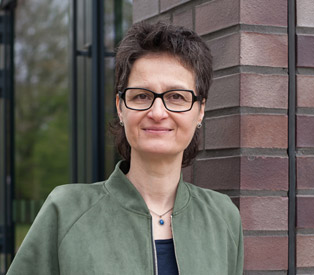 Rabea Wienholt steht in einer grünen Jacke vor einer Backsteinmauer mit einem Glasfenster.